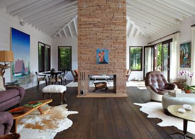 A two-story stone fireplace divides the living room. The art is by Dirk Skreber, left wall, George Condo, fireplace, and Herman Bas, right wall. The coffee table, left foreground, is by George Nakashima. Vintage American armchairs covered in linen, below, are beneath a Massimo Vitali photograph in the master bedroom. A two-story stone fireplace divides the living room. The art is by Dirk Skreber, left wall, George Condo, fireplace, and Herman Bas, right wall. The coffee table, left foreground, is by George Nakashima. Vintage American armchairs covered in linen, below, are beneath a Massimo Vitali photograph in the master bedroom.