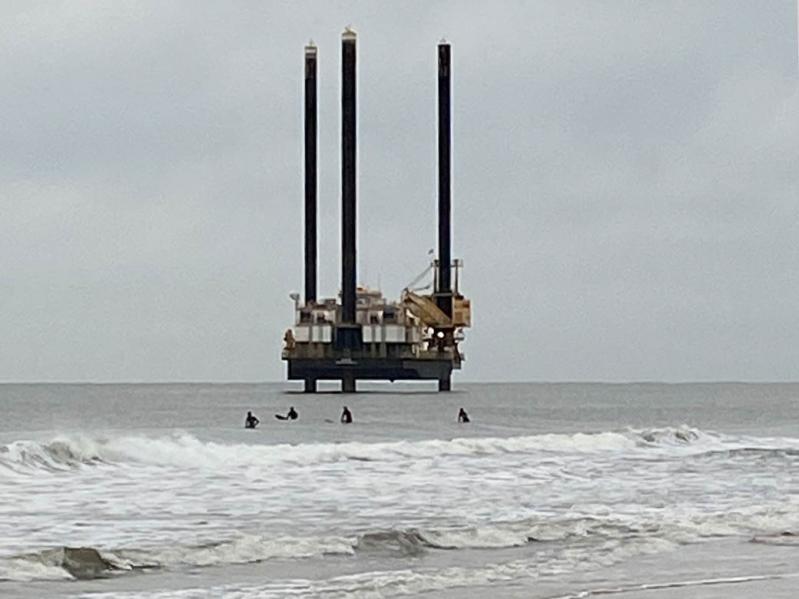 Surfers near Georgica Beach dwarfed by an exploratory driling rig taking sea-floor samples in preparation for a planned electric cable installation